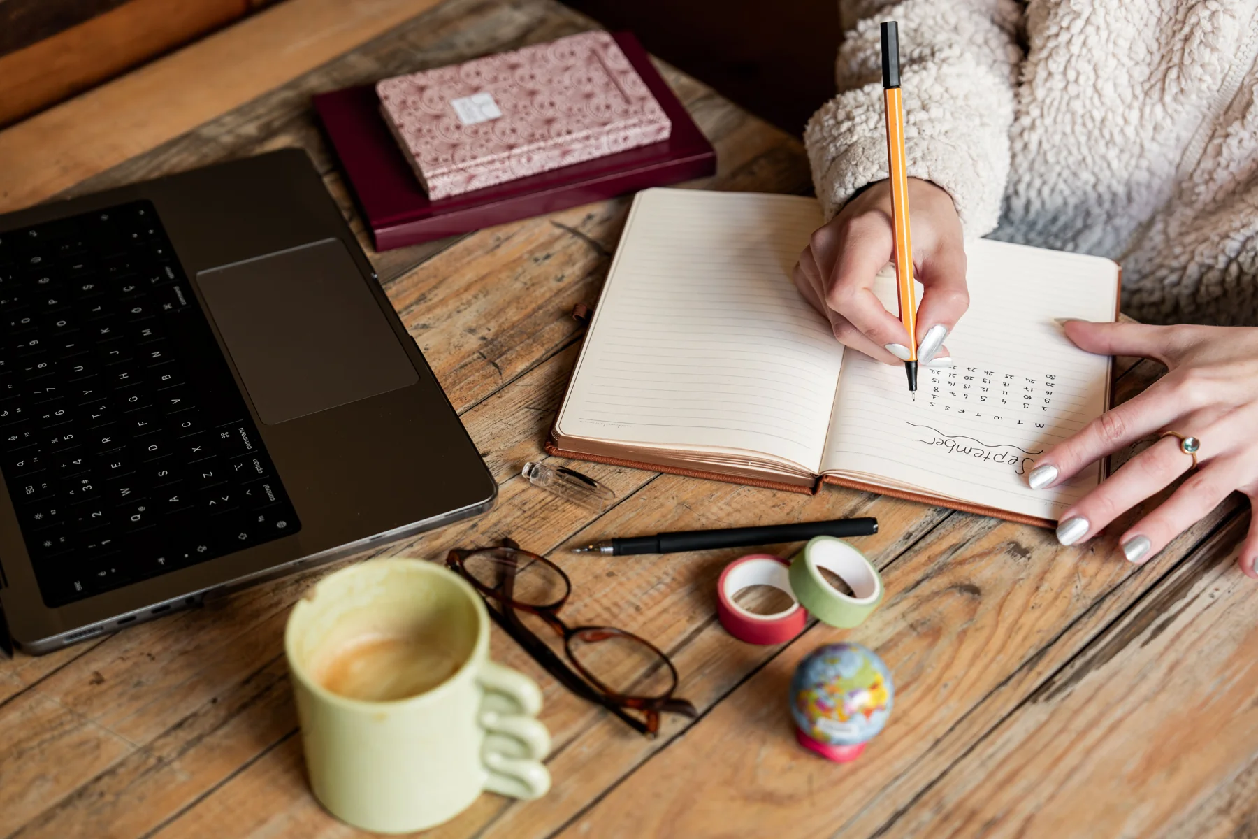 Woman planning her schedule in a notebook beside a laptop and coffee